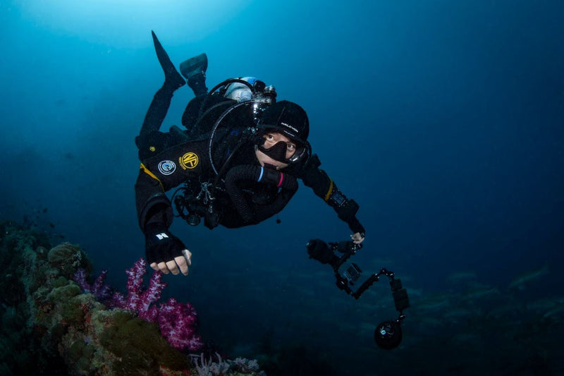 A technical diver in a Navyfel drysuit with a camera rig swimming past soft coral