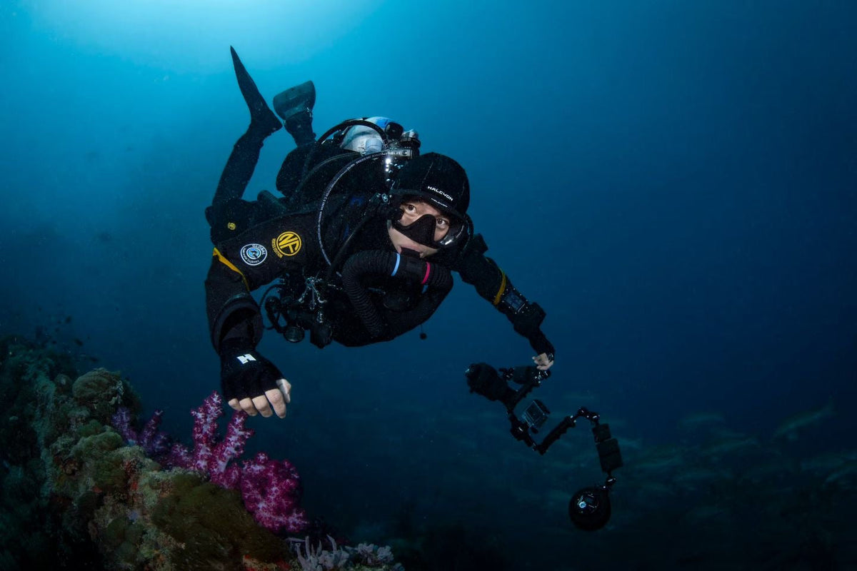A technical diver in a Navyfel drysuit with a camera rig swimming past soft coral