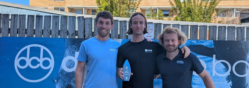 Three Dive Centre Bondi team members holding the PADI Outstanding Contribution to Diver Education award in front of the dcb banner