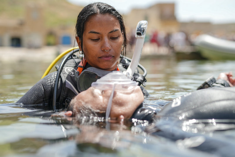 A Rescue Diver student giving rescue breaths through a pocket mask to an unresponsive diver at the surface